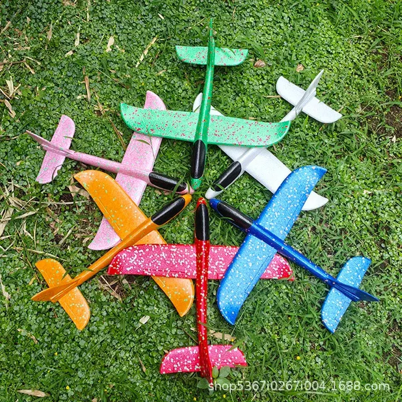 Top-down view of six colorful hand throwing glider planes scattered on green grass